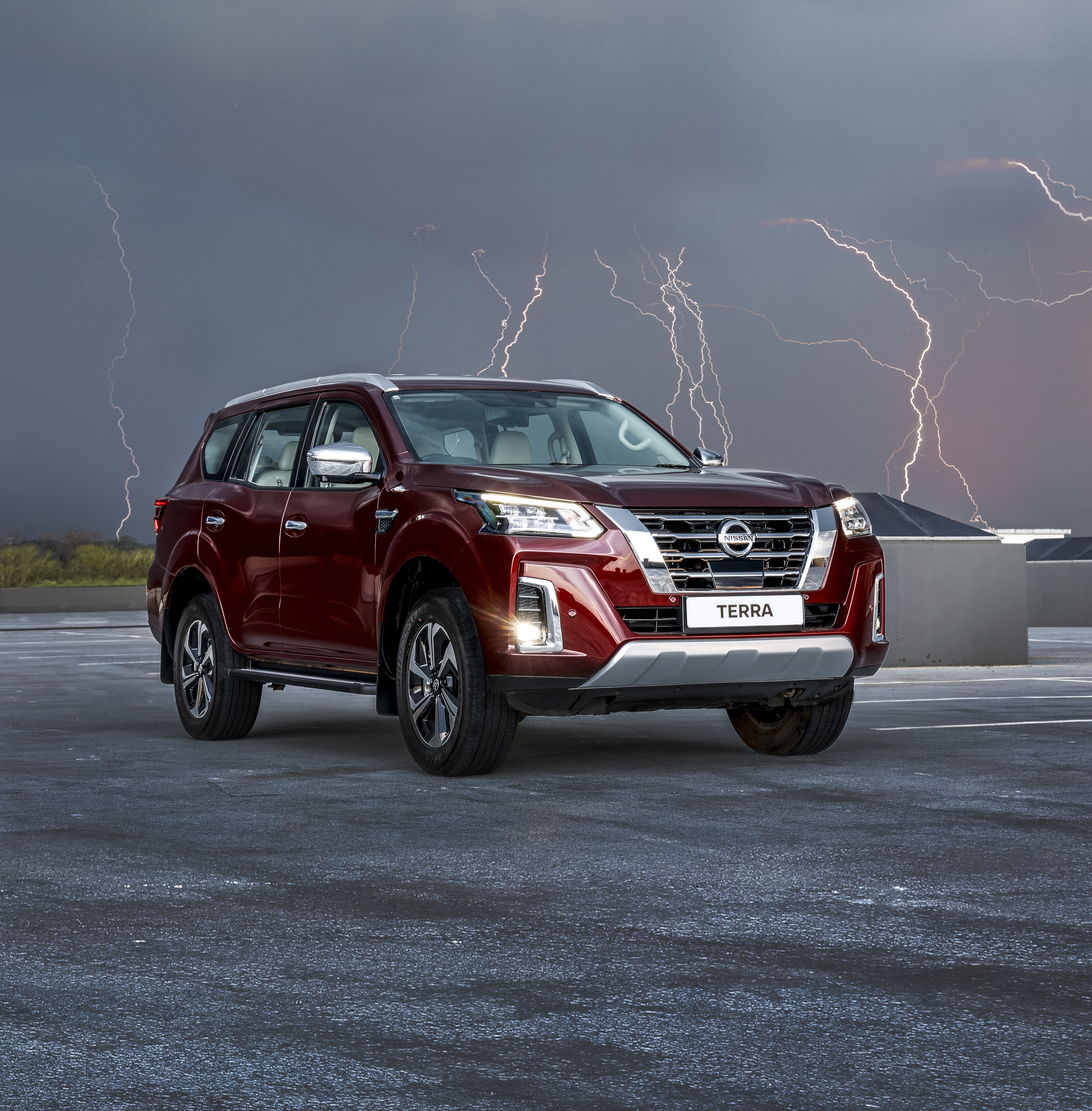 Red Nissan Terra in open field with lighting in background